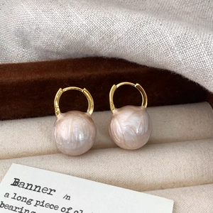 Detail of gold hoop earrings with large champagne marble pearls on beige velvet