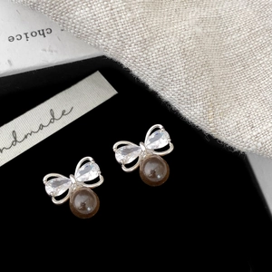 Detail of silver bow earrings with clear zircons and brown round tiger eye bead charm