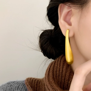 Minimalist long teardrop earrings with matte gold satin finish shown on a model