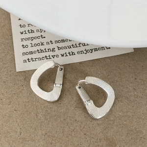 Detail of silver teardrop earrings featuring brushed metal texture and geometric design