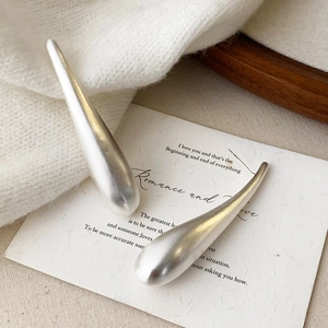 Close-up of matte silver brushed teardrop earrings on white card and wood tray