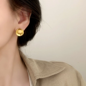 Minimalist brushed gold disc stud earrings with smooth matte texture worn by a model