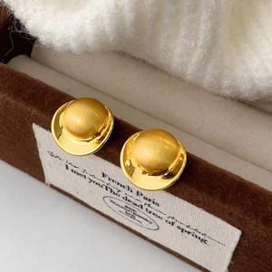 Close-up of matte brushed gold stud earrings with layered semi-sphere design on velvet box