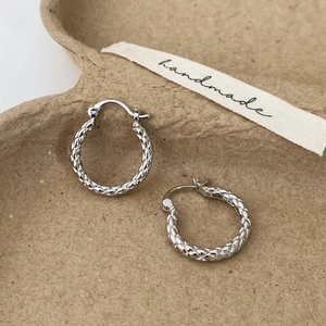 Macro detail of silver-colored hoop earrings featuring a woven geometric texture on a tray