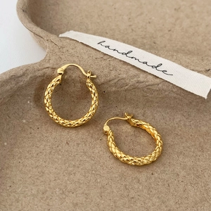 Close-up of golden hoop earrings featuring intricate woven textures and handmade details