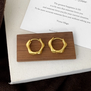 Detail of matte gold wavy hoop earrings with brushed texture on a wooden pedestal