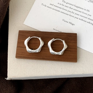 Detailed view of silver irregular brushed hoop earrings on a minimalist wooden stand
