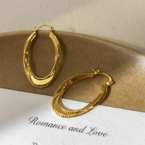 Detail of twisted gold-plated geometric hoop earrings with polished surface and beaded edge