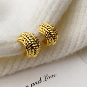 Boucles d'oreilles créoles torsadées dorées sur fond de tricot blanc élégant