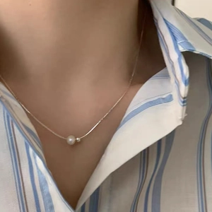 Elegant silver snake chain necklace with a round freshwater pearl on a blue striped shirt