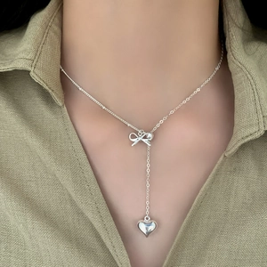 Elegant silver bow and heart pendant Y-necklace worn on model with green shirt