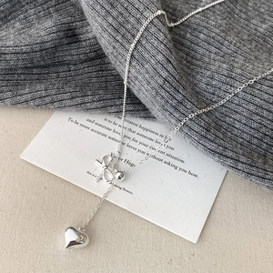 Elegant silver bow and heart necklace displayed on a cozy knit background
