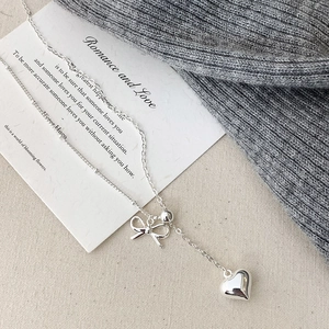 Silver bow and heart pendant necklace displayed on an elegant textured fabric background