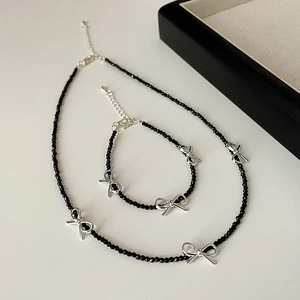 Minimalist black beaded necklace and bracelet set with silver bow charms on white background