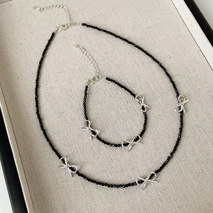 Bowknot beaded necklace and bracelet set with black spinels on a beige jewelry display tray