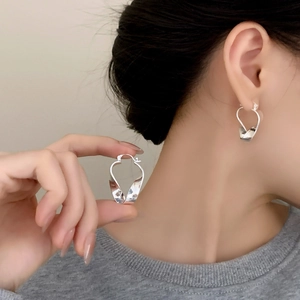 Polished silver twisted heart earrings with minimalist geometric design on model