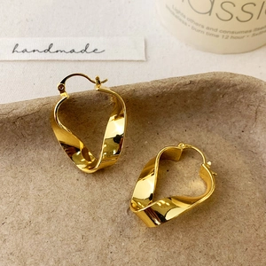 Macro view of gold-plated twisted geometric hoop earrings on a minimalist tray