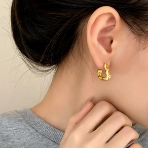 Close-up of elegant gold pleated irregular geometric C-shaped stud earrings on model