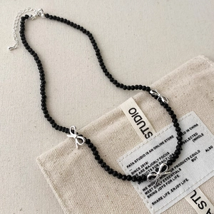 Black beaded necklace with silver bow charms on a minimalist beige canvas bag