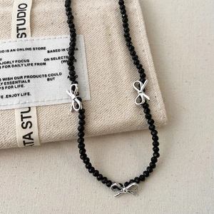 Minimalist beaded necklace featuring black faceted beads and silver bow pendants on canvas