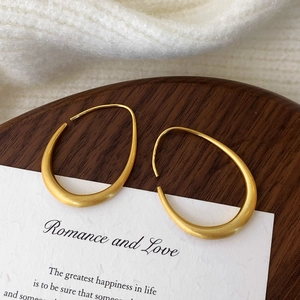 Macro view of matte brushed gold geometric earrings in irregular drop shape on wood and card