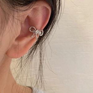 Elegante ear cuff in argento a forma di fiocco indossato da una donna in stile minimal