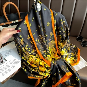 Detail of luxury black silk-feel scarf with orange edges and elegant floral patterns