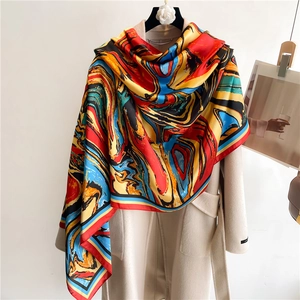 Artistic abstract silk scarf with vibrant marble patterns draped over a beige coat