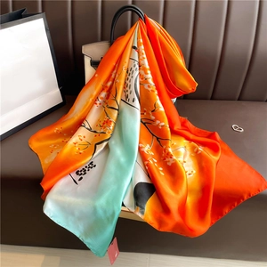 Detail of floral silk scarf draped on a beige bag with orange and green floral patterns