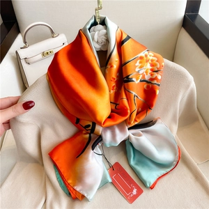 Detailed view of silk-texture floral scarf in vibrant orange and green with soft drape