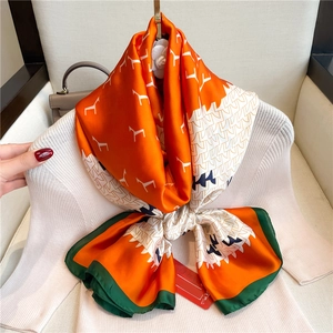 Detail of luxury orange silk scarf with horse print and dark green border over a knit top