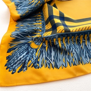 Detail of yellow silk scarf with blue tassel print and fine stitching on twill fabric