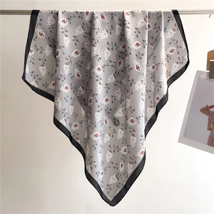 Detail of square silk scarf showing grey paisley pattern and contrasting black borders