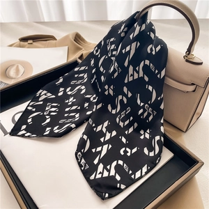 Detail of black and white geometric letter print satin scarf tied on a beige handbag