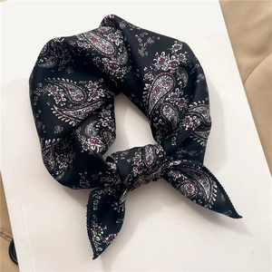 Detailed view of paisley pattern on a black satin silk neck scarf tied in a bow
