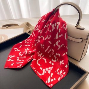 Elegant red satin silk scarf with geometric letters tied on a beige luxury handbag