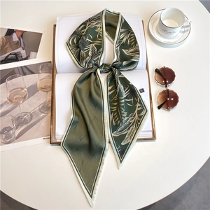 Elegant dark green satin scarf with palm leaf print on a white book with sunglasses