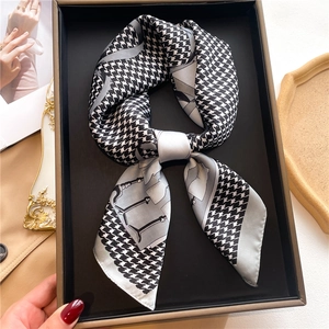 Detail of houndstooth silk-like scarf tied in a bow inside a premium black gift box