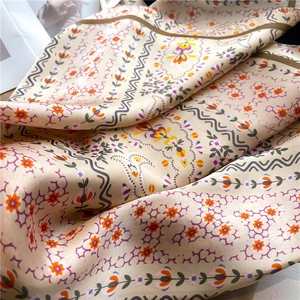 Close-up of floral satin scarf with elegant orange flowers on smooth gold fabric