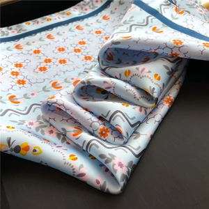 Detail of floral silk scarf showing light blue fabric with orange flowers and dark navy hem
