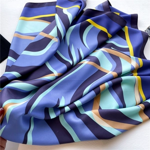 Detailed view of large square silk scarf with blue geometric wave patterns and silky texture