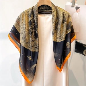 Détail d'un foulard en satin soyeux avec imprimés planétaires dorés et bordure orange