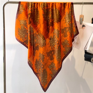 Detailed close-up of orange faux silk scarf with floral patterns hanging on metal rack