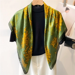 Detail of green floral silk scarf with golden pattern draped on a black mannequin