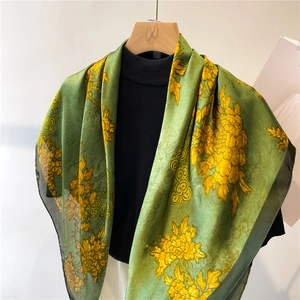 Detail of silk-feel scarf featuring yellow chrysanthemums and cloud patterns on green