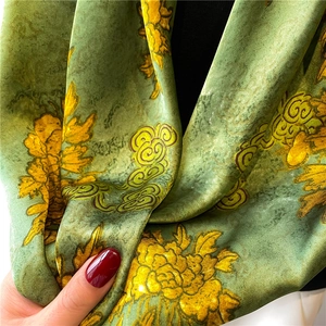 Detailed view of green silk scarf with yellow floral and cloud patterns draped on neck