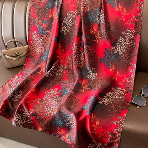 Luxurious long silk scarf with red floral print draped elegantly on a leather sofa