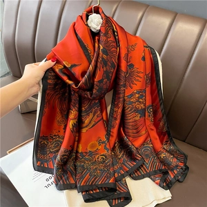 Luxurious long silk-feel scarf with red phoenix pattern and black border draped over hands