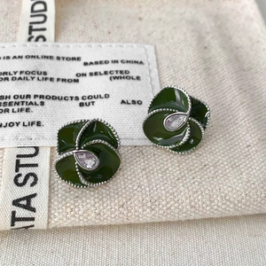 Detail of dark green petal earrings with teardrop zircon on a textured canvas background