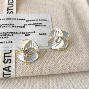 Close-up of vintage flower earrings with white petals and gold beaded edges on canvas bag